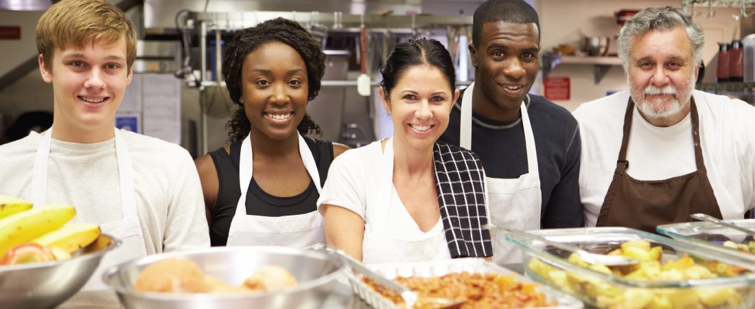 Diverse group of volunteers in kitchen smiling with meal they all helped to prepare